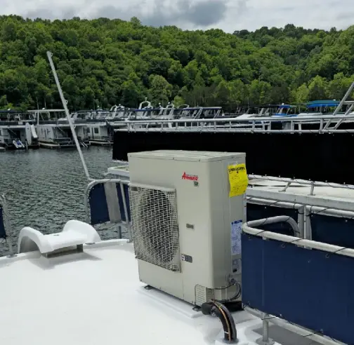 An air conditioning unit installed on a boat deck, surrounded by a marina with boats and lush green hills in the background